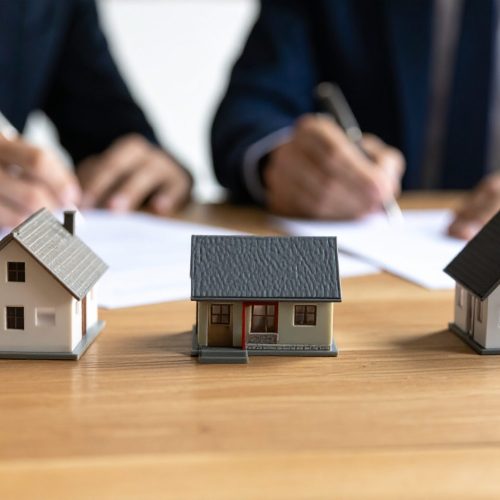 Real estate deal signing with miniature houses, property investment concept, home buying agreement, mortgage loan application, financial planning