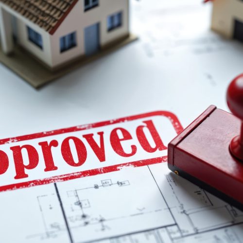 Architectural blueprint displays house models with approved stamp. Pencil and brush sit on drawings, signifying successful project planning.